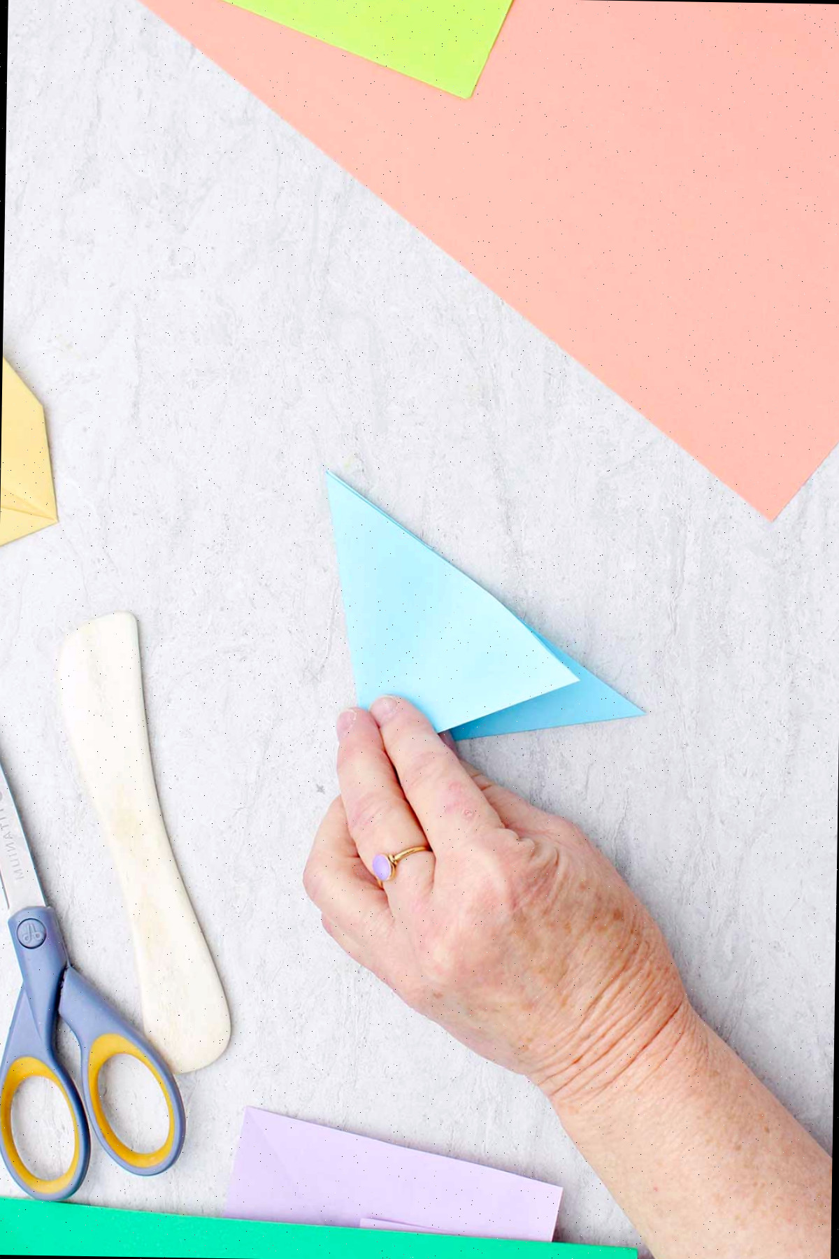 Uma pessoa dobrando um pedaço de papel azul claro para criar uma flor.