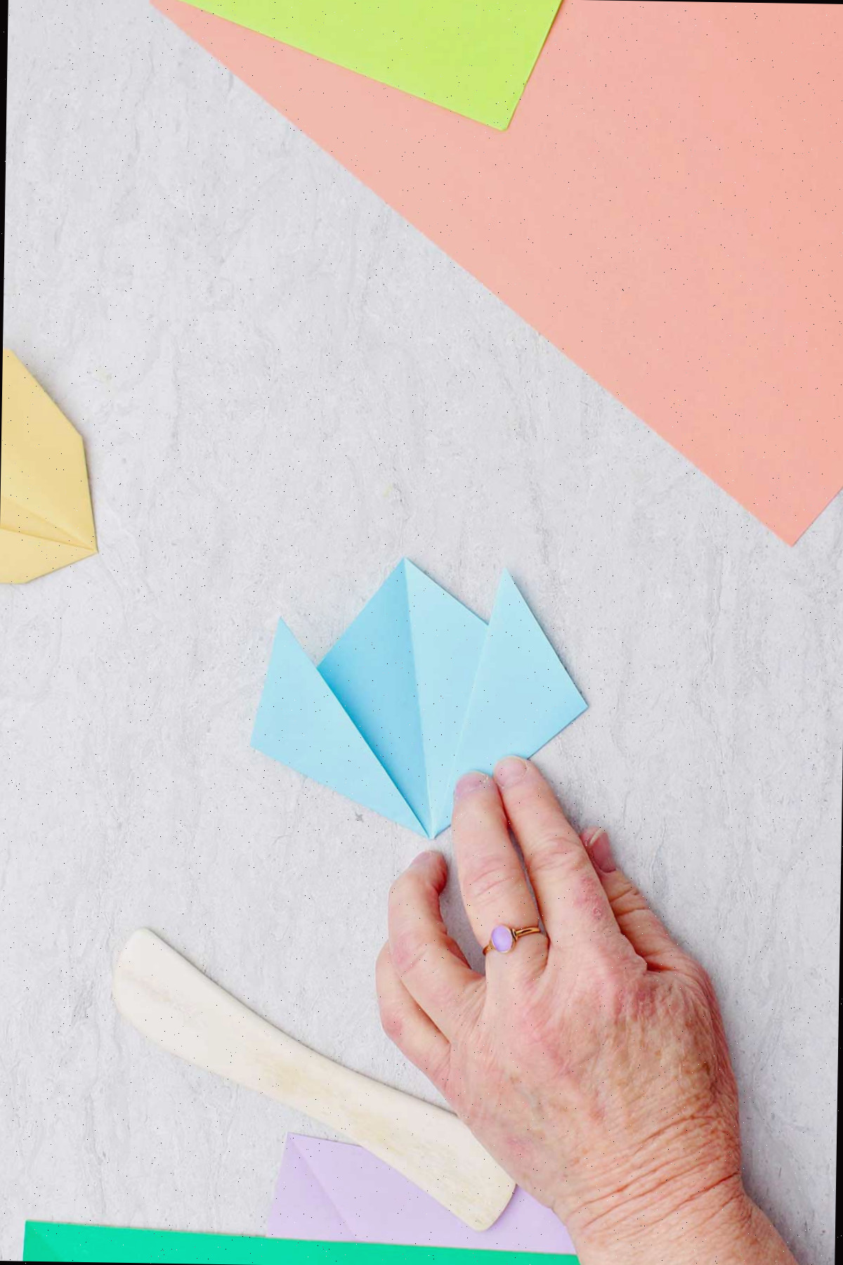 Uma pessoa dobrando um pedaço de papel azul claro para criar uma flor.