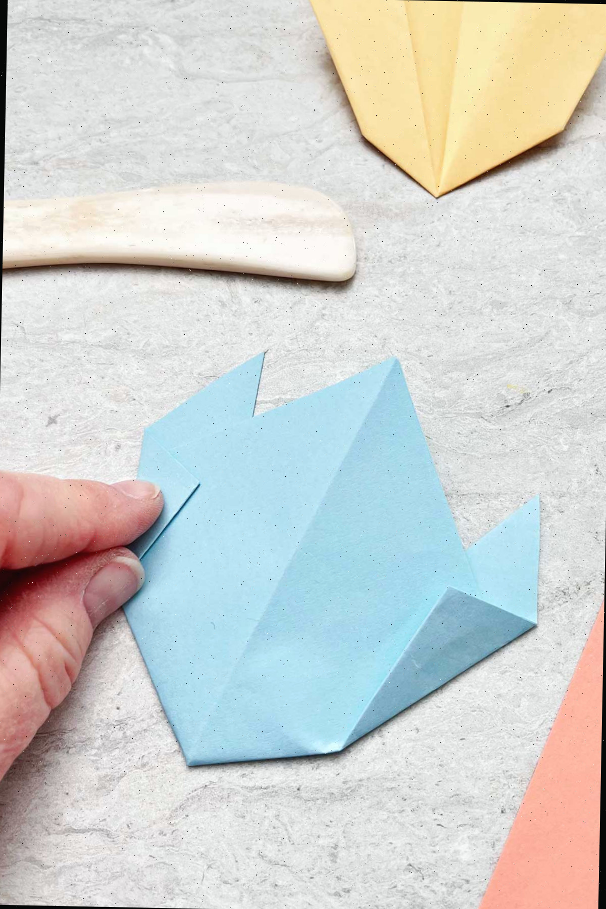Uma pessoa dobrando um pedaço de papel azul claro para criar uma flor.