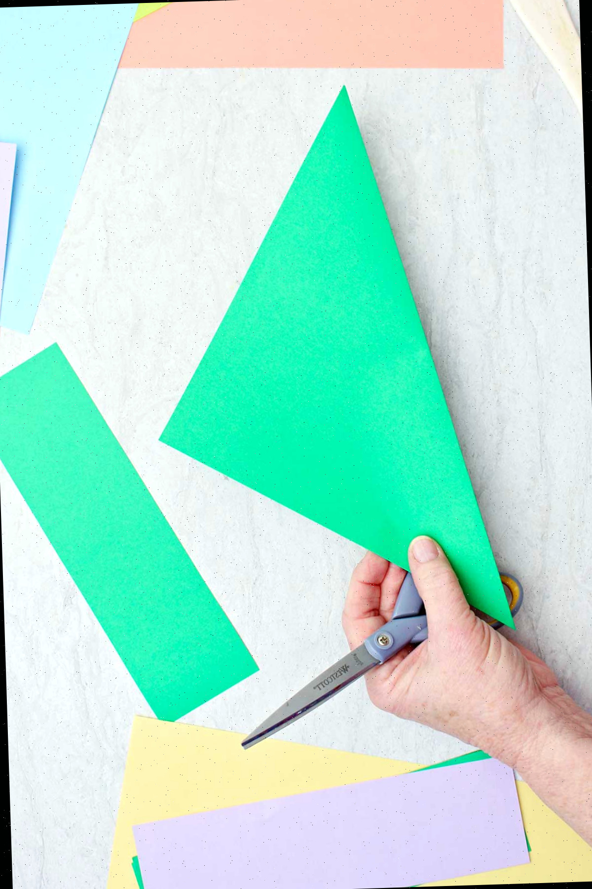 Uma pessoa cortando um pedaço de papel verde para criar um caule de flor de origami.