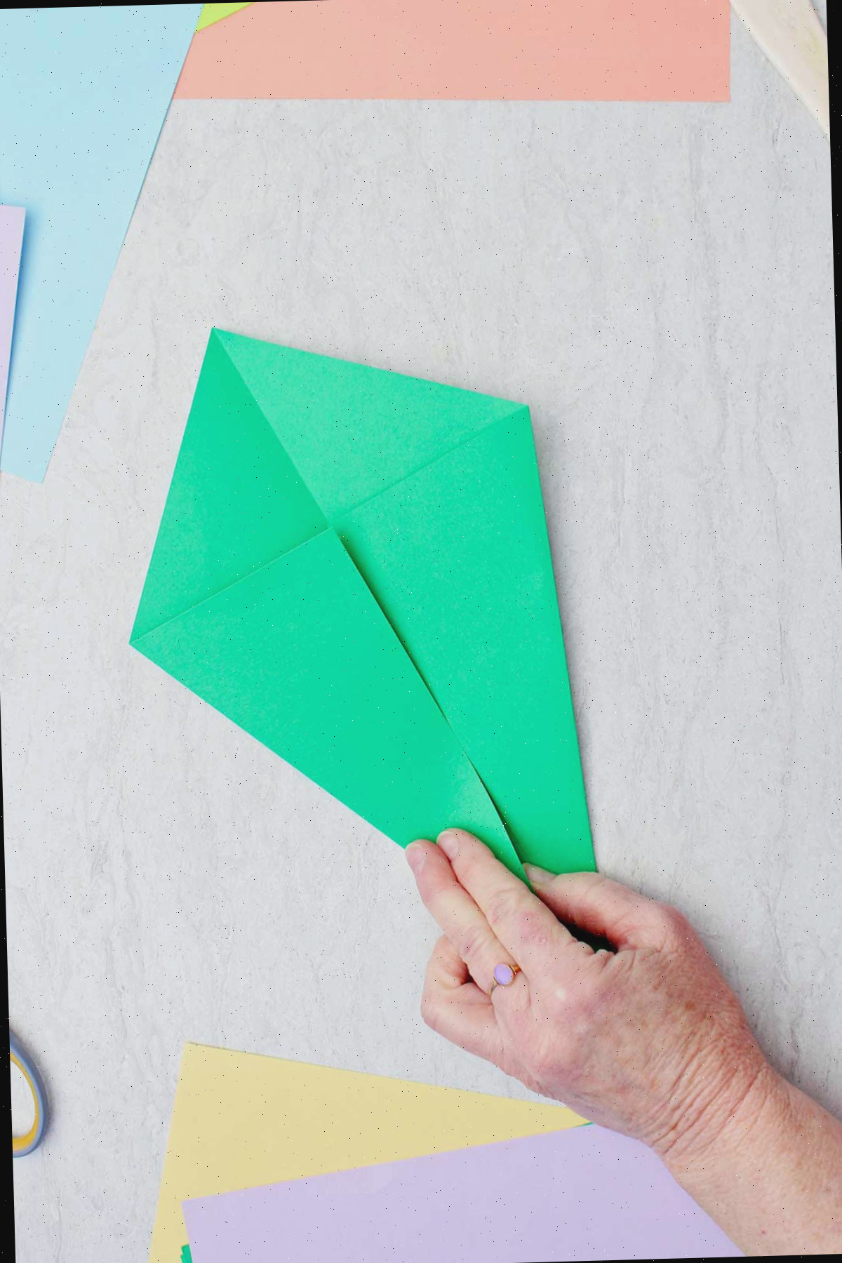 Uma pessoa dobrando um pedaço de papel verde para criar um caule de origami.