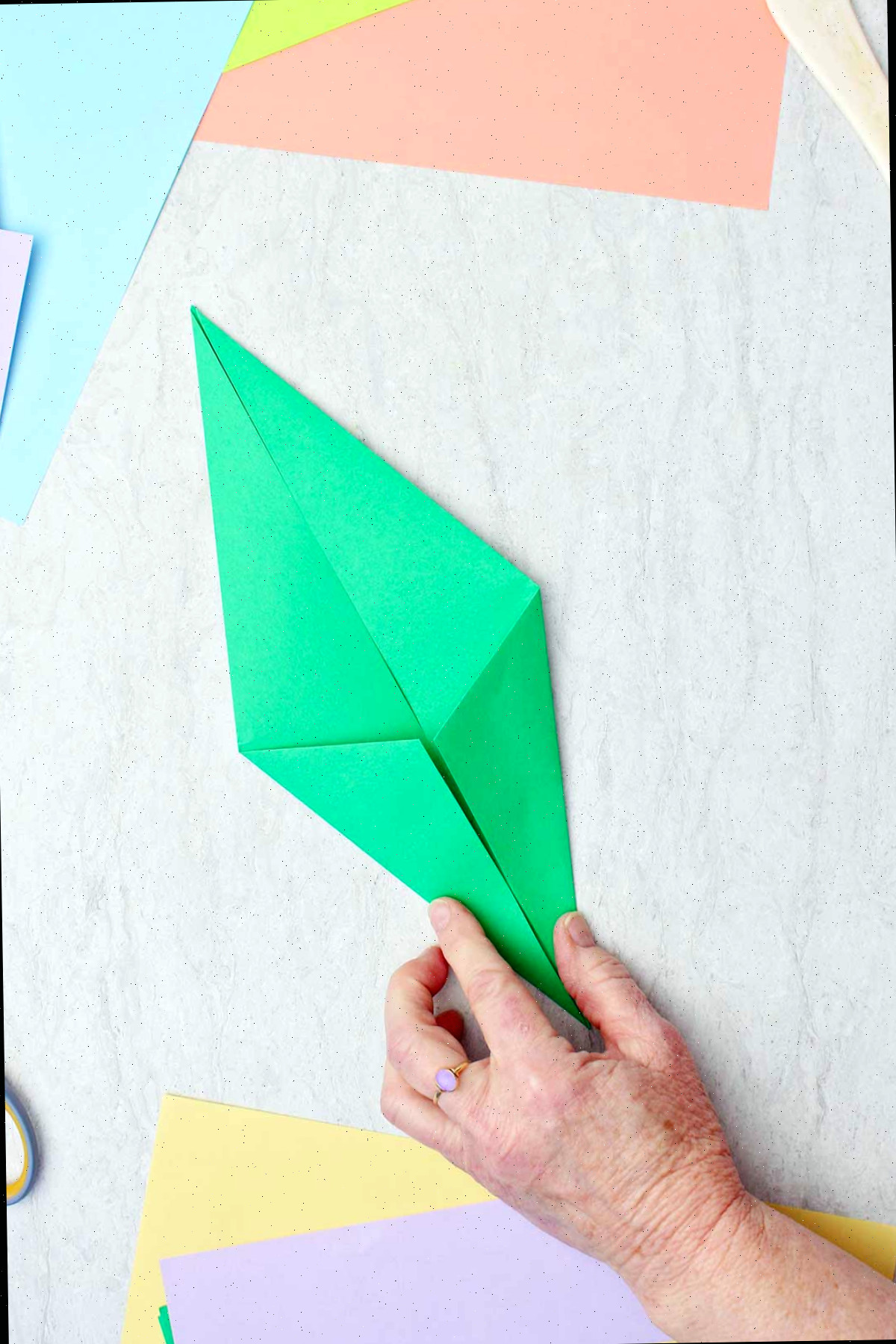 Uma pessoa dobrando um pedaço de papel verde para fazer um caule de origami.