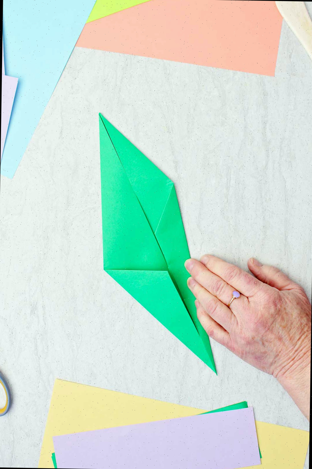 Uma pessoa dobrando um pedaço de papel verde para fazer um caule de origami.