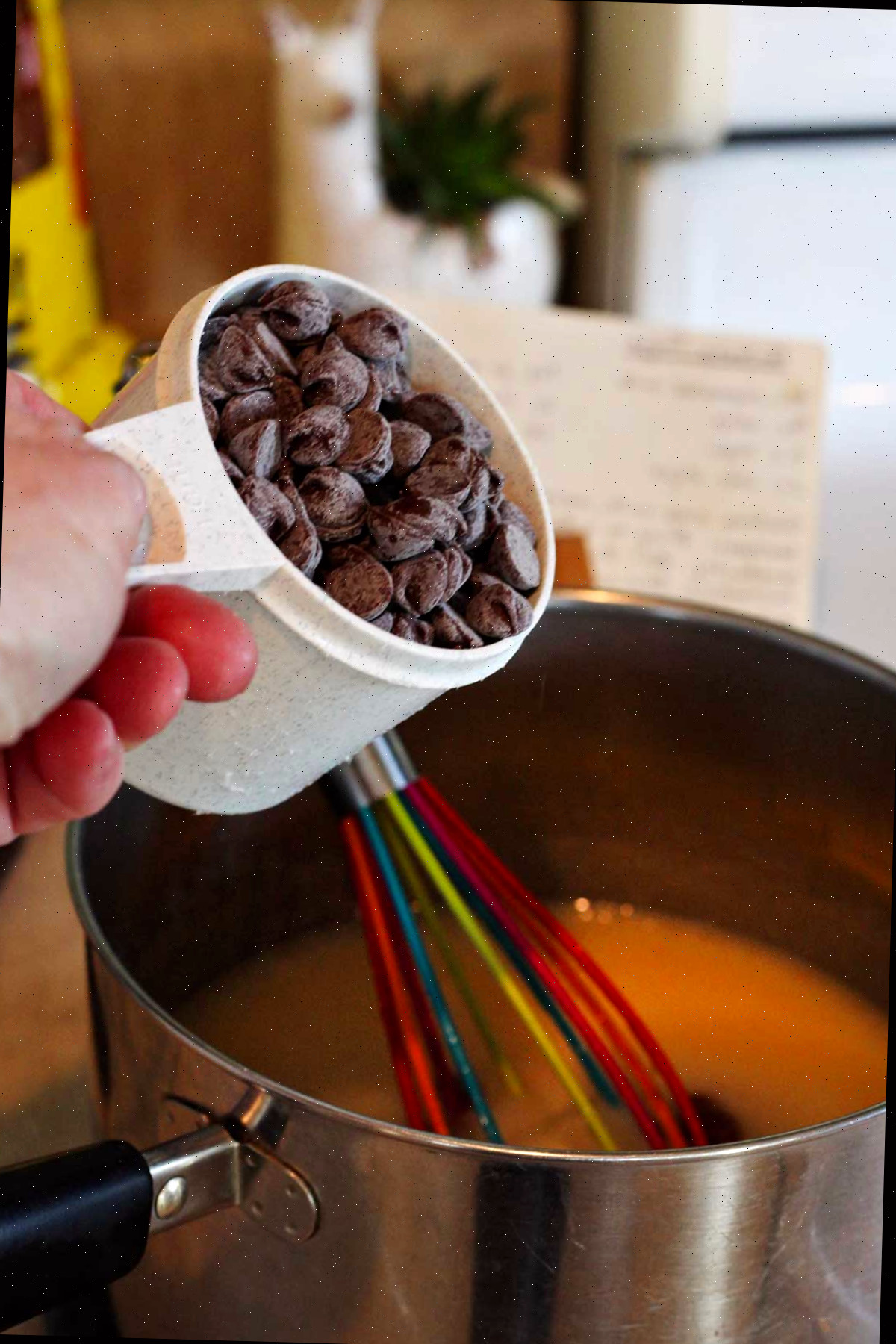 Uma pessoa prestes a adicionar uma xícara de gotas de chocolate à mistura de fudge na panela.