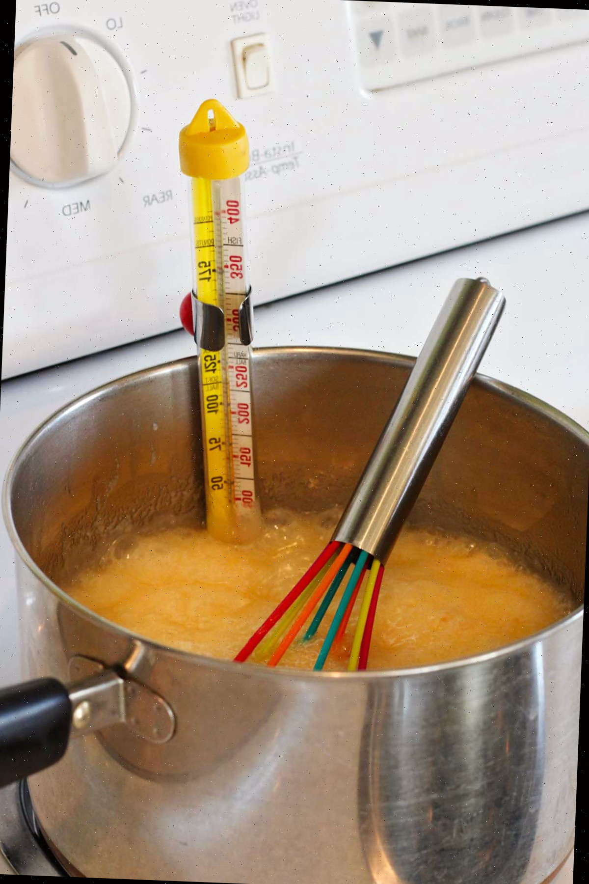 Mistura de fudge fervendo no fogão com um termômetro de doces medindo a temperatura.