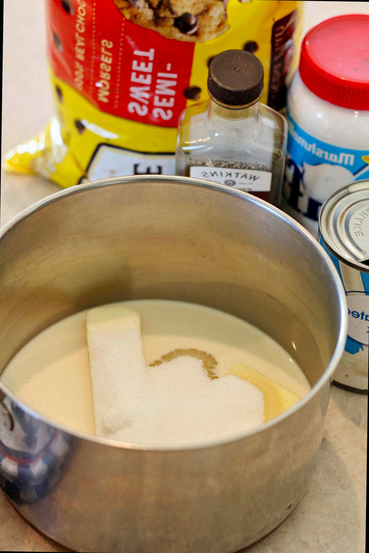 Uma panela cheia de leite evaporado, manteiga e açúcar com outros ingredientes ao fundo.