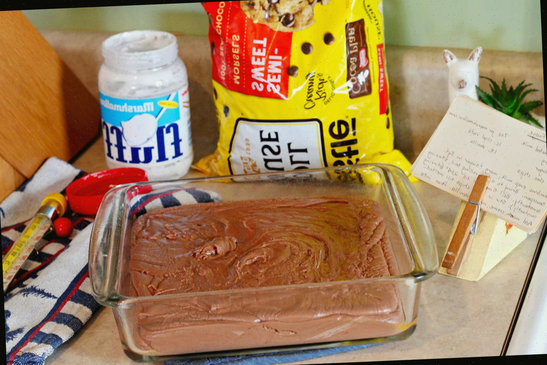 Mistura de fudge na forma de vidro sobre a bancada com chips de chocolate, fluff e receita perto.