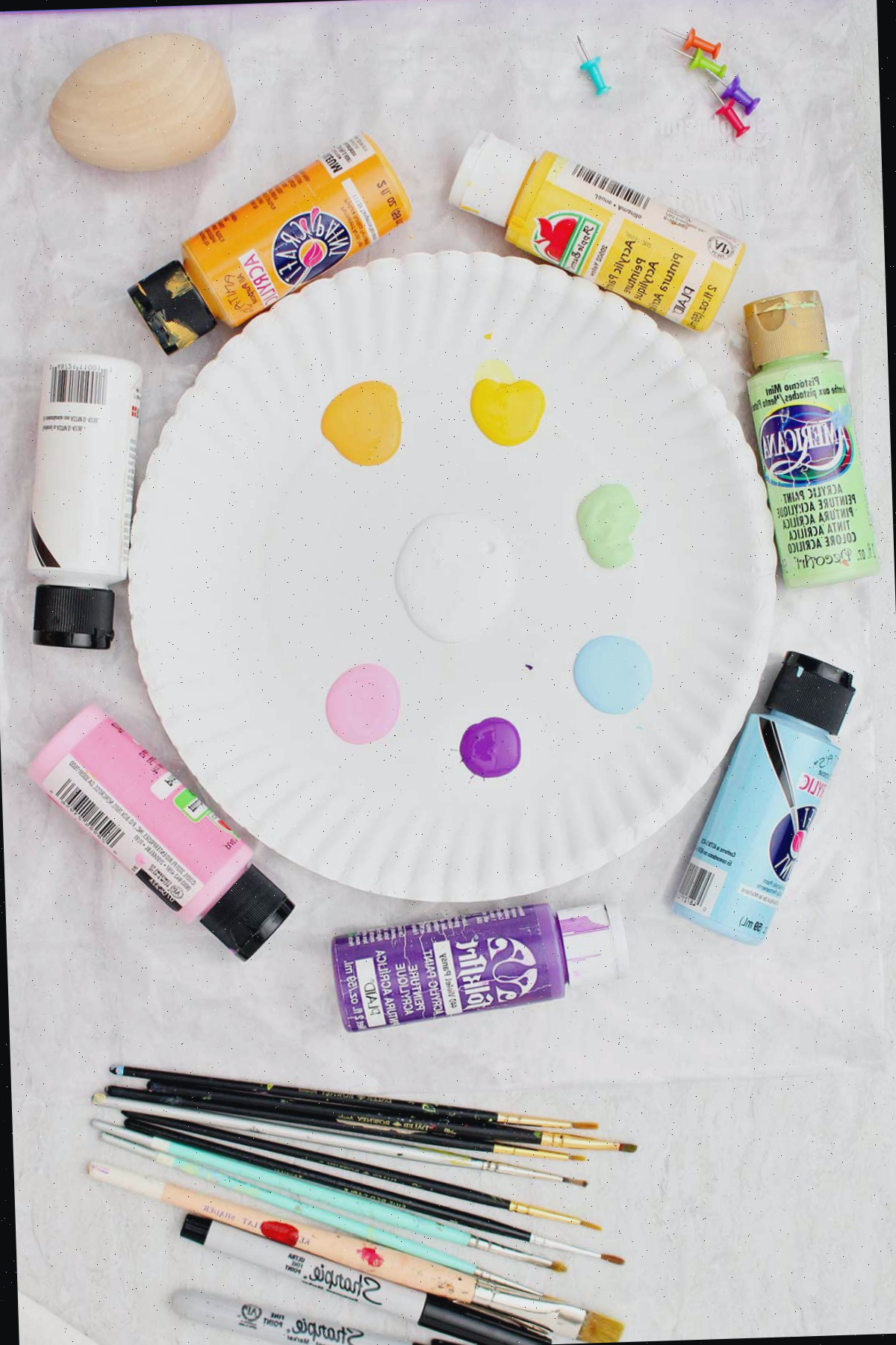 Um prato de papel contendo diversas cores de tinta acrílica, pincéis e tintas acrílicas.