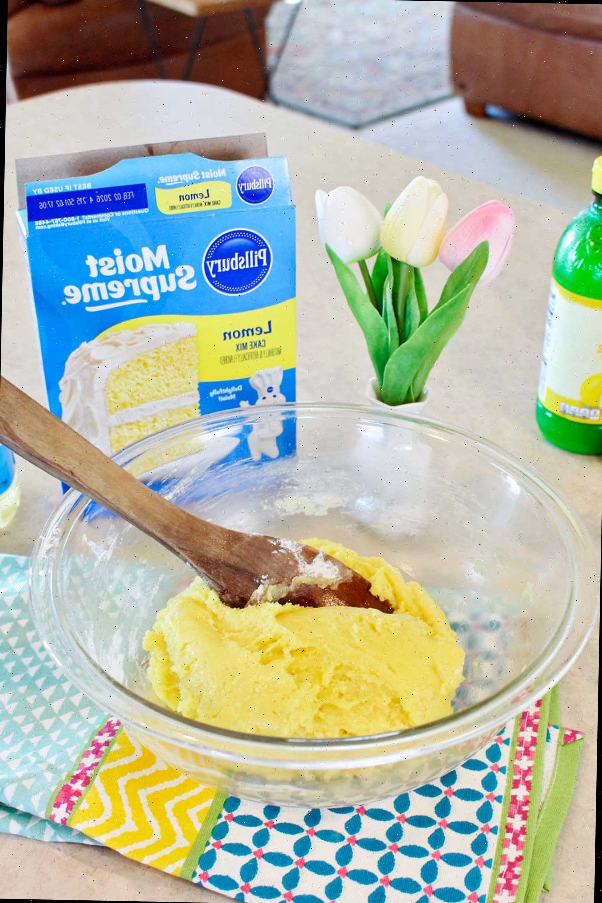 Massa de bolo de limão misturada em uma tigela com ingredientes e tulipas ao fundo.