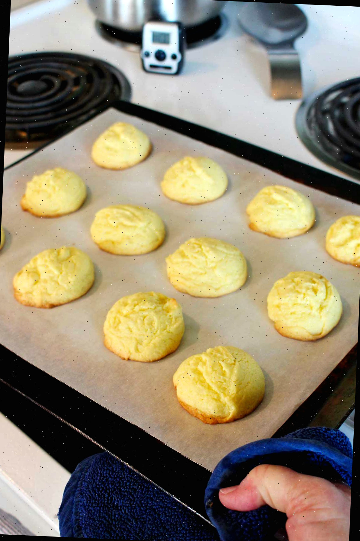Uma pessoa retirando uma assadeira com biscoitos de bolo de limão assados do forno.