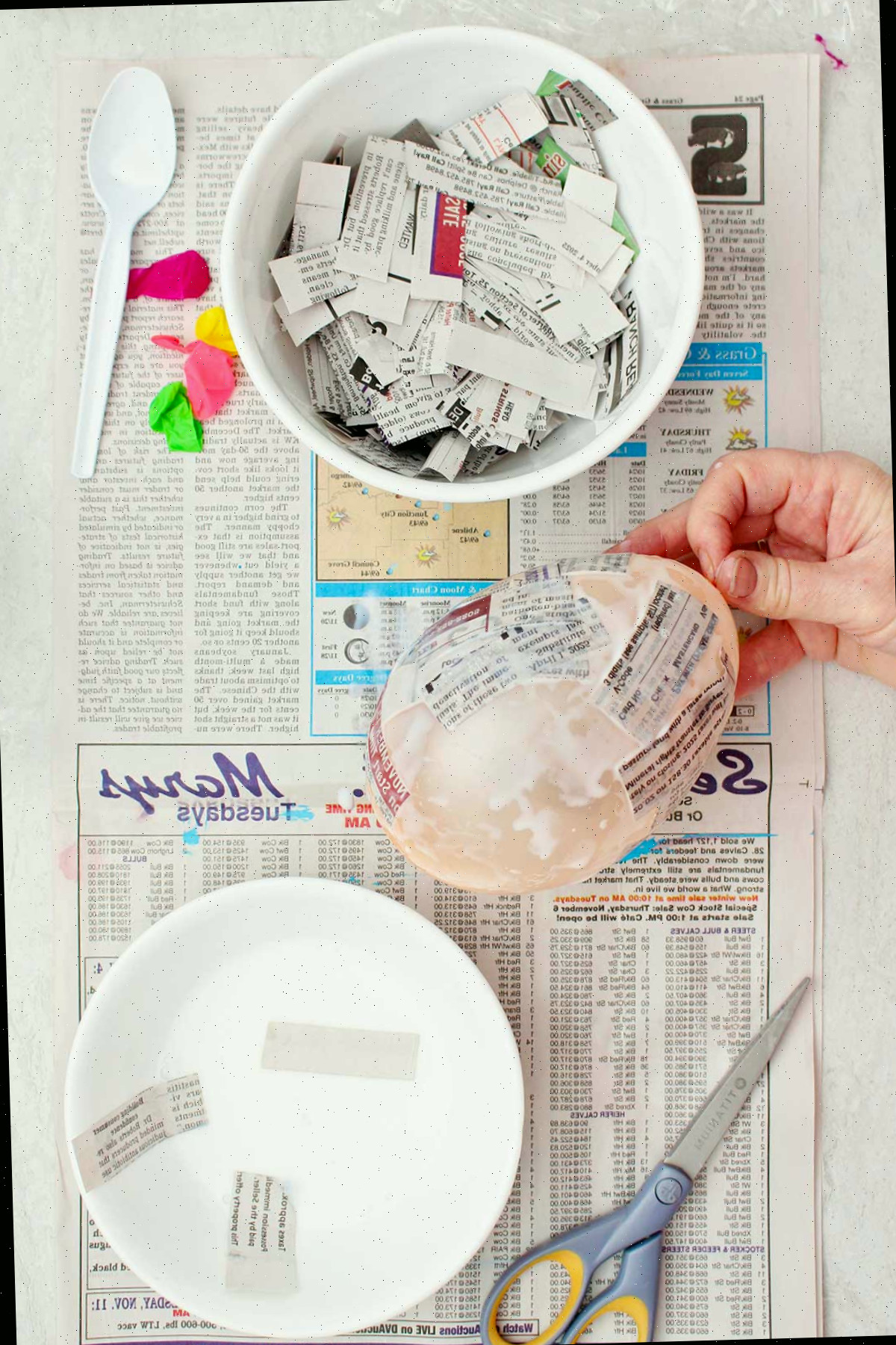 Uma pessoa segurando um pequeno balão sendo utilizado como molde para um projeto de papel machê.