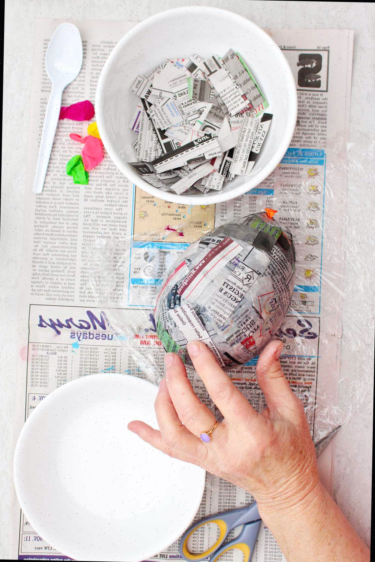Uma pessoa pressionando pedaços de papel machê sobre um balão devidamente inflado.