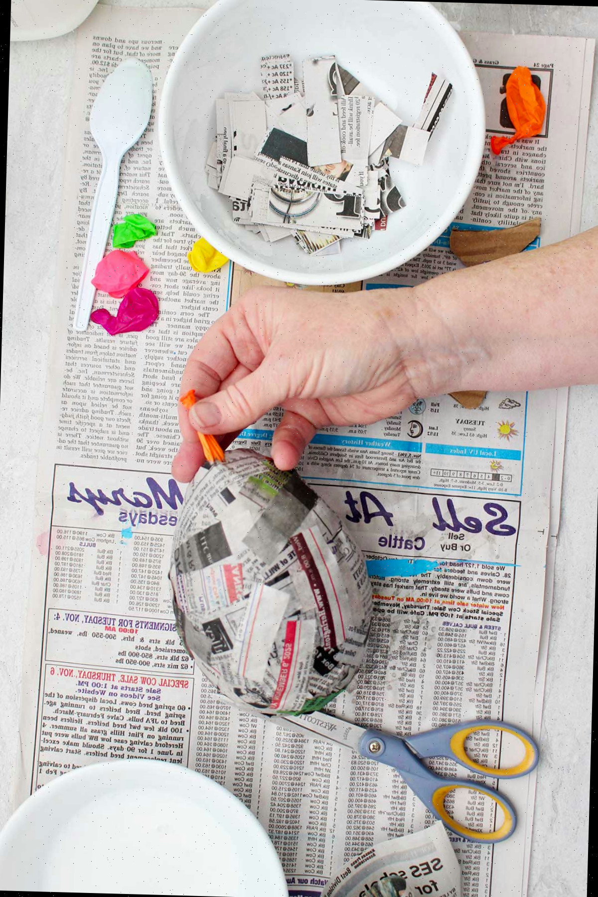 Uma pessoa removendo um balão estourado de um projeto de papel machê seco.
