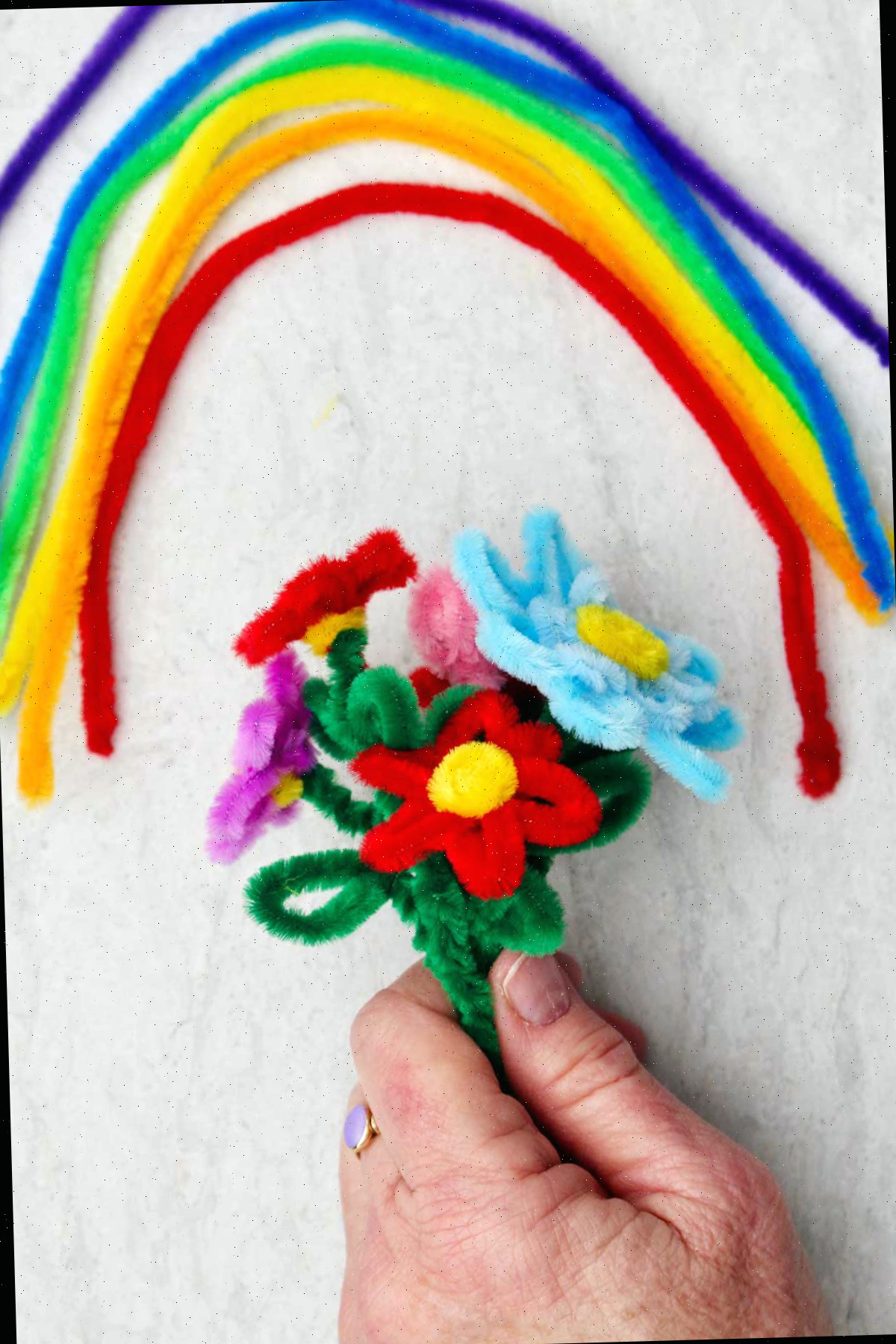 Uma pessoa segurando um buquê de flores de limpadores de pipe em várias cores com um arco-íris de limpadores de pipe acima.