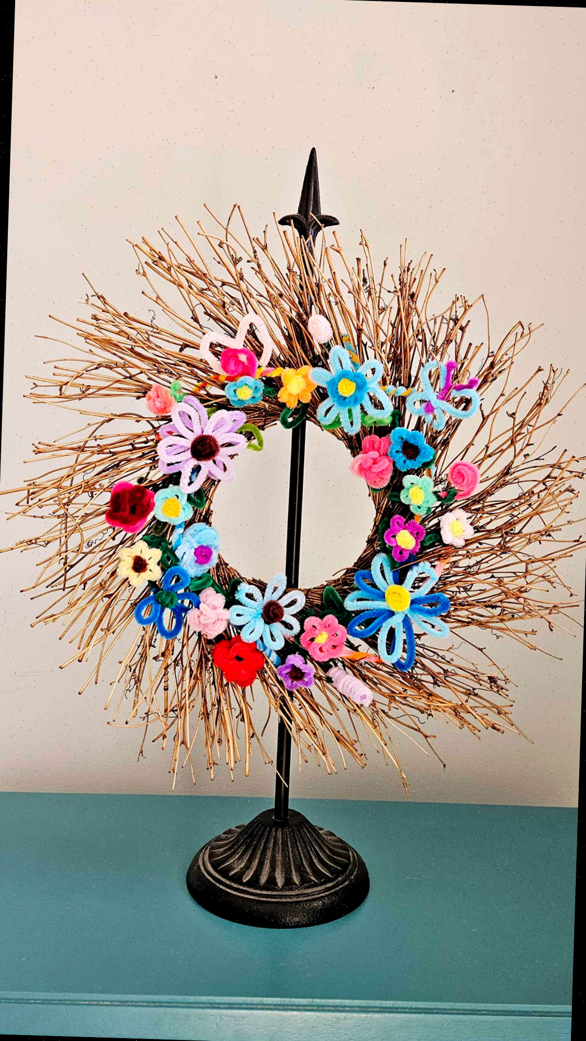 Uma guirlanda de galhos em um suporte com flores de limpador de pipe multicoloridas anexadas.