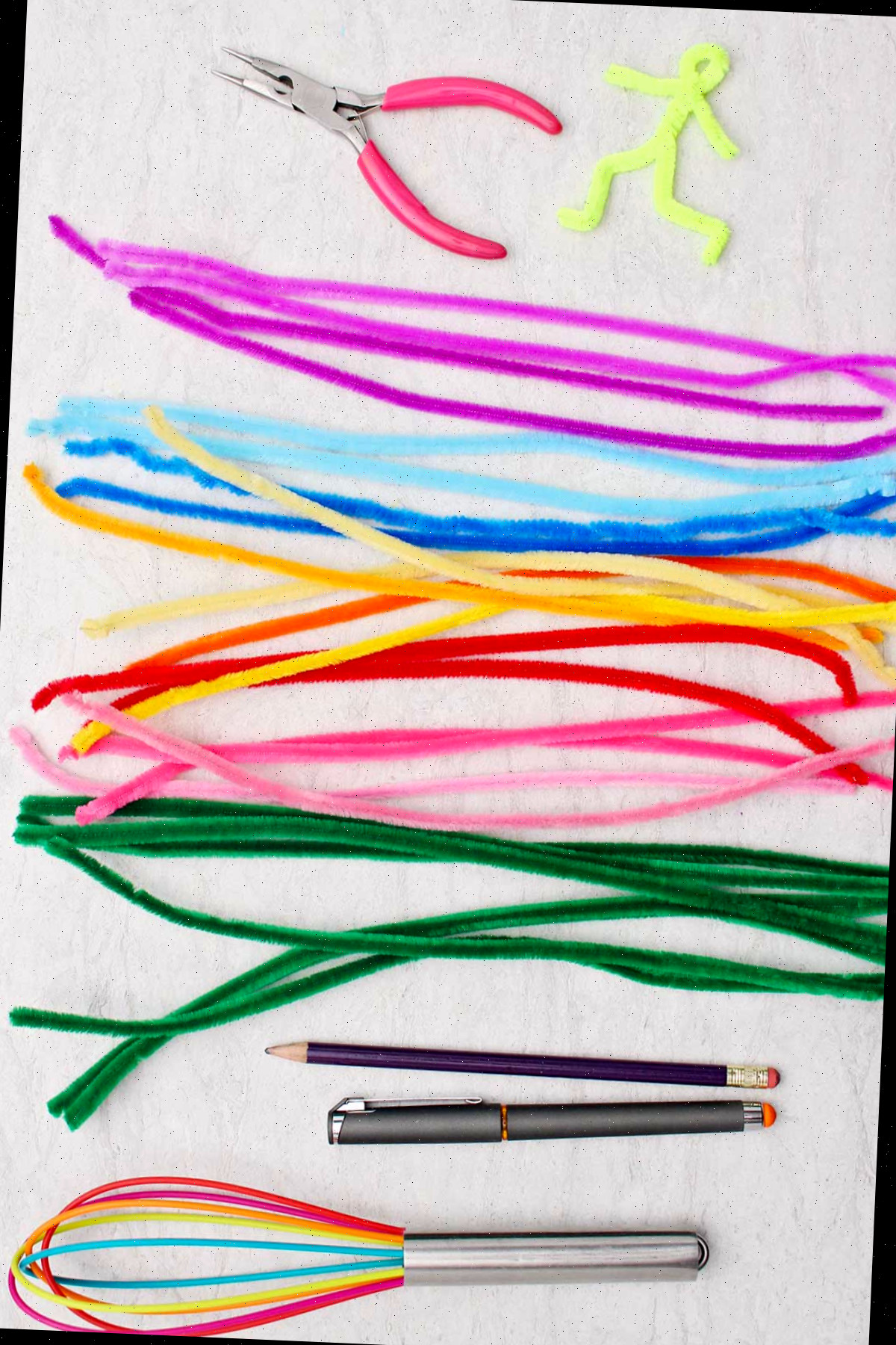 Um conjunto de limpadores de tubo coloridos, um batedor multicolorido, uma caneta, um lápis e alicates de ponta fina.