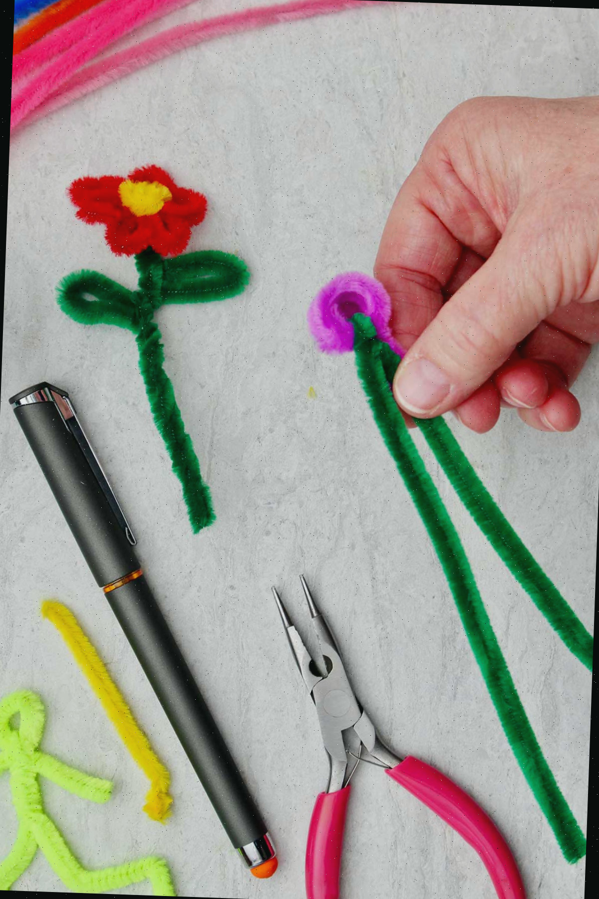 Uma pessoa segurando o início de uma flor de limpador de tubo com caule verde e outros materiais por perto.