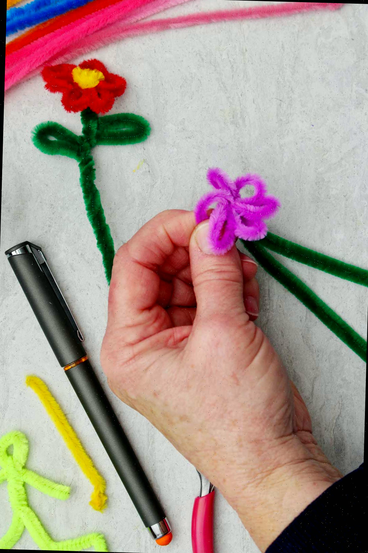 Pessoa segurando a flor de limpador de pipe enquanto cria as pétalas roxas.
