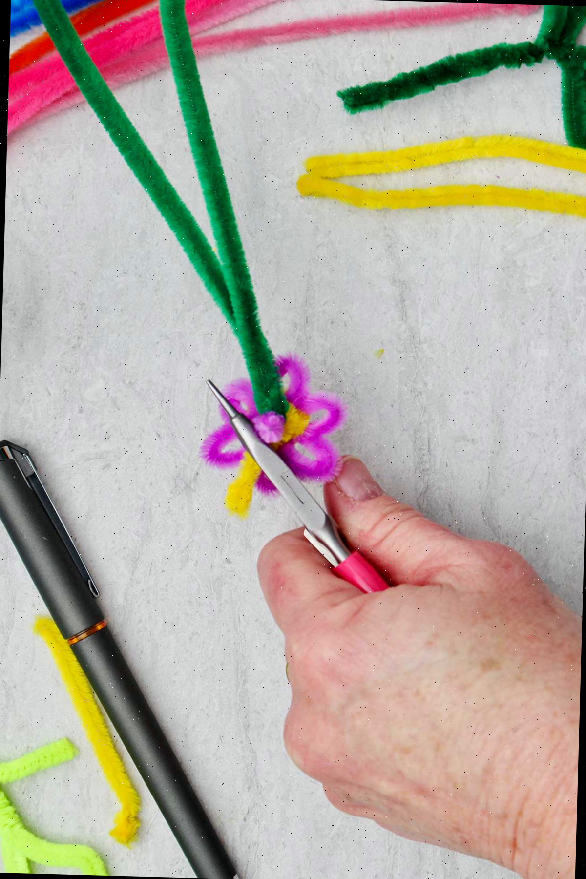 Uma pessoa dobrando e aparando o excesso de limpador de pipe amarelo na parte de trás da flor.