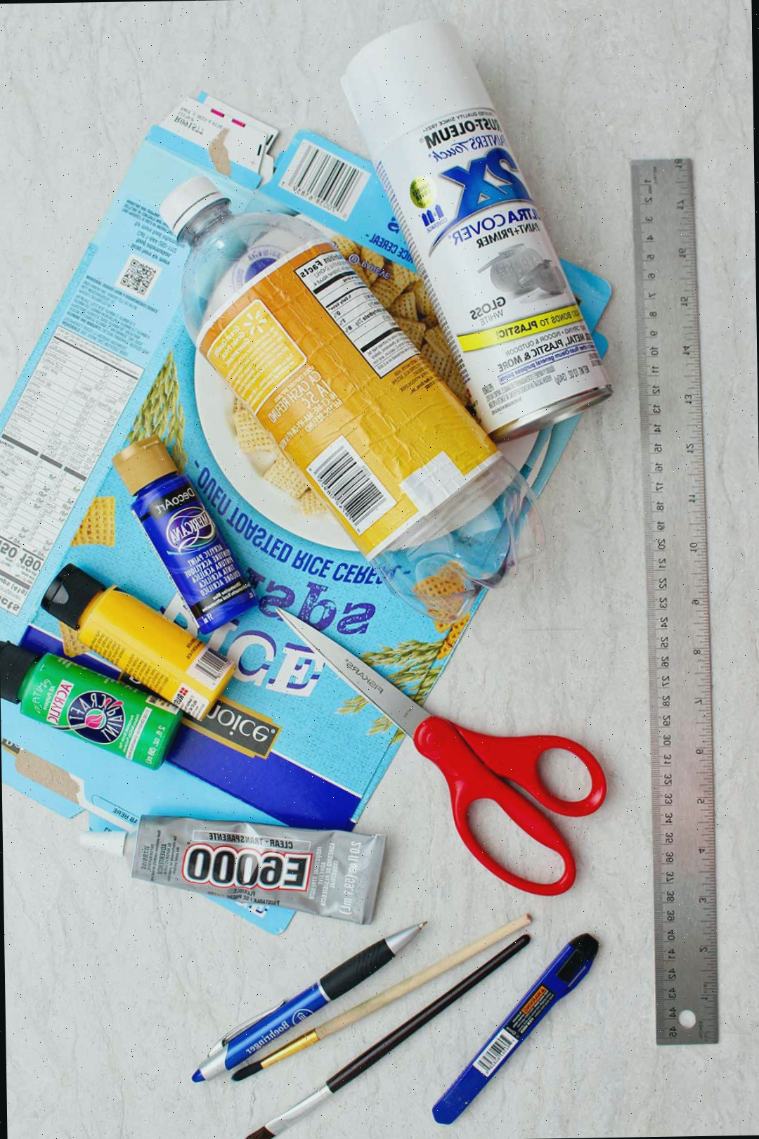 Materiais para um avião de garrafa plástica. Tinta spray branca, garrafa plástica de refrigerante vazia, caixa de cereal de papelão achatada, tintas, tesoura, régua e cola.