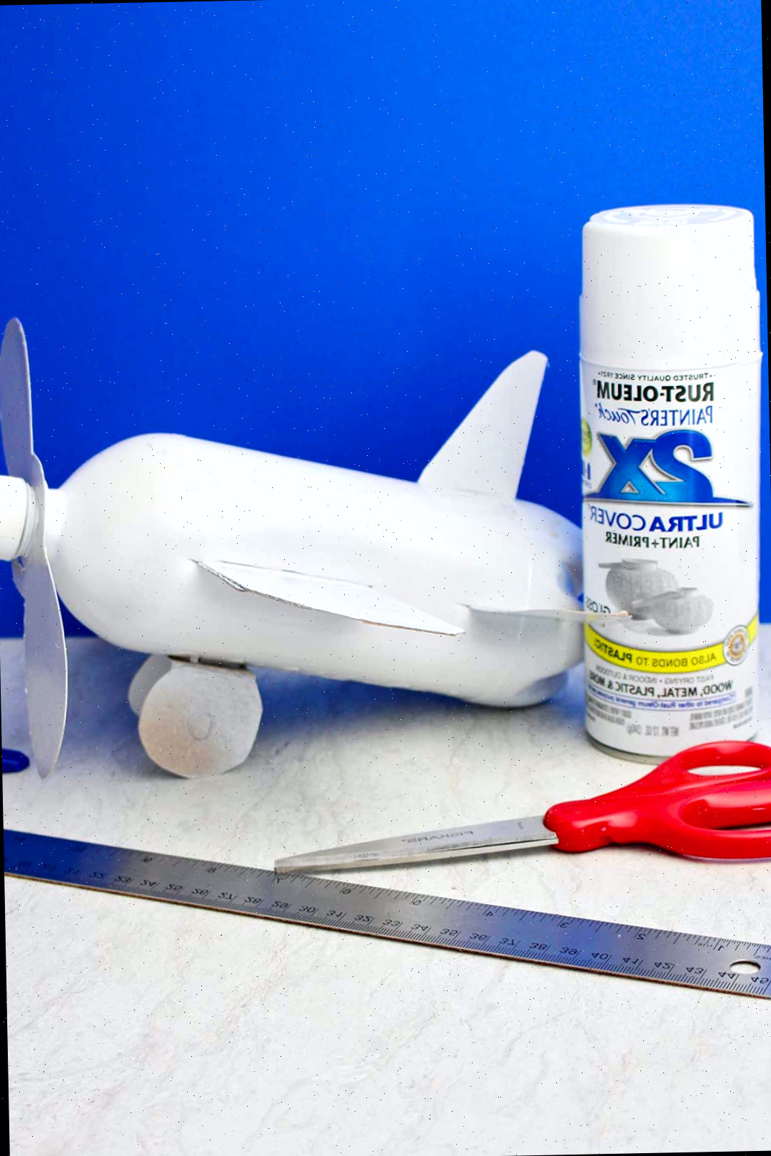 Avião de garrafa pintado com spray branco contra fundo azul.