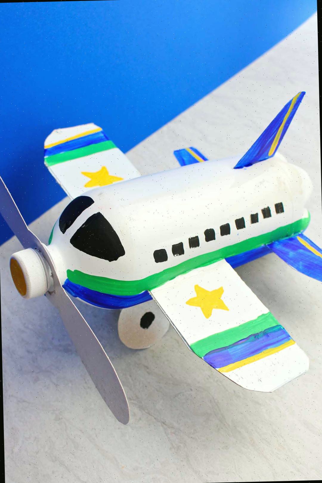 Vista de cima de um projeto de avião feito de garrafa completamente pintado e finalizado contra um fundo azul.