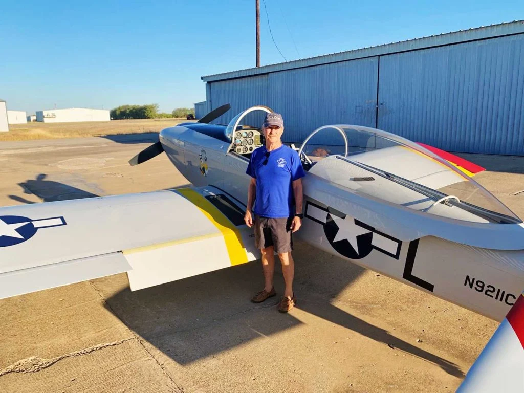 Homem usando camisa azul diante de um pequeno avião de um passageiro do lado de fora.