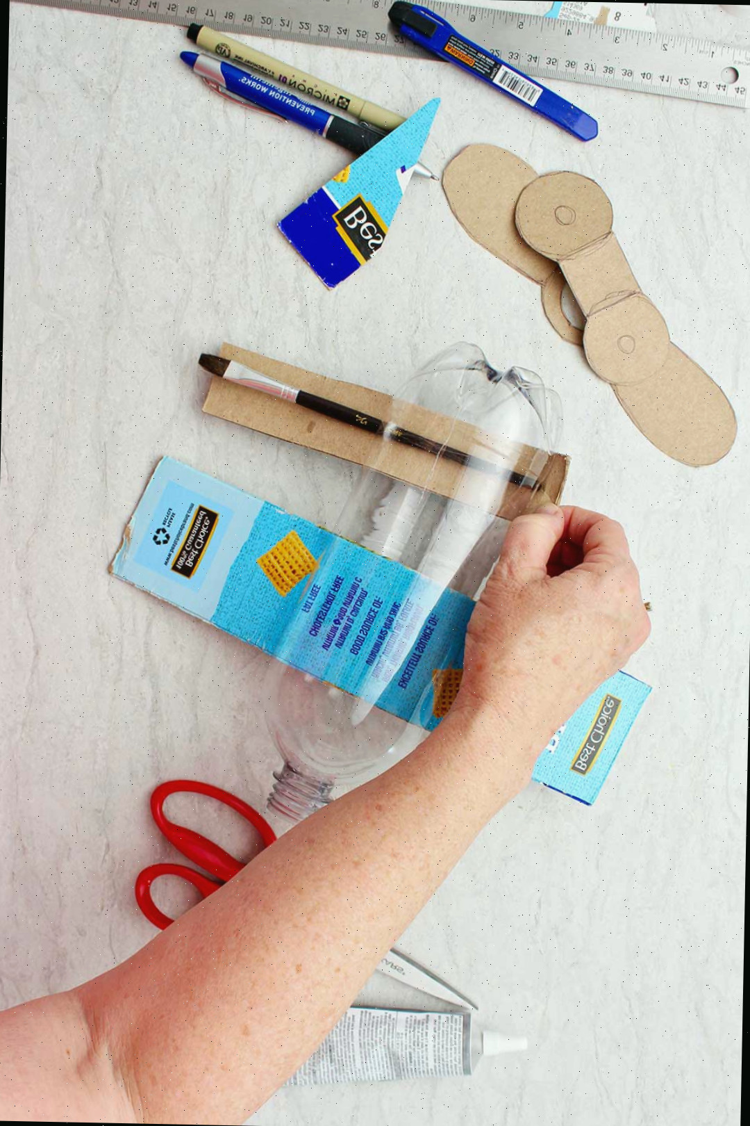 Mão puxando retângulo de papelão (asas) através de fenda na garrafa.