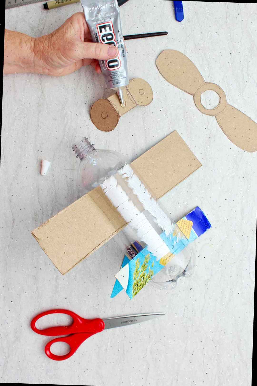Mão colando peças de papelão cortadas para se assemelhar a rodas na parte inferior da garrafa.