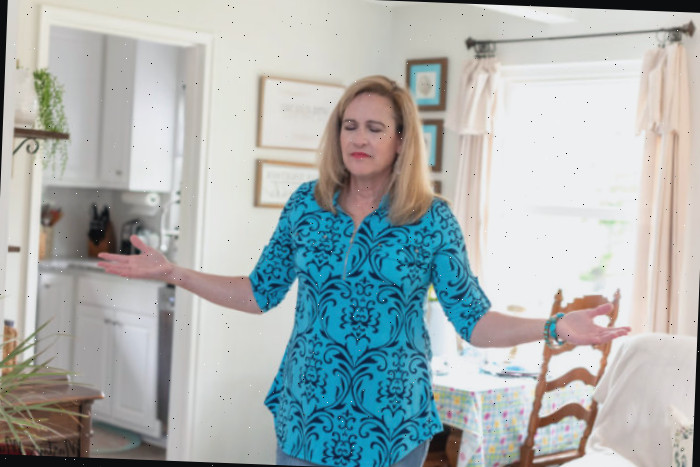 Mulher orando com as mãos estendidas em uma casa pequena