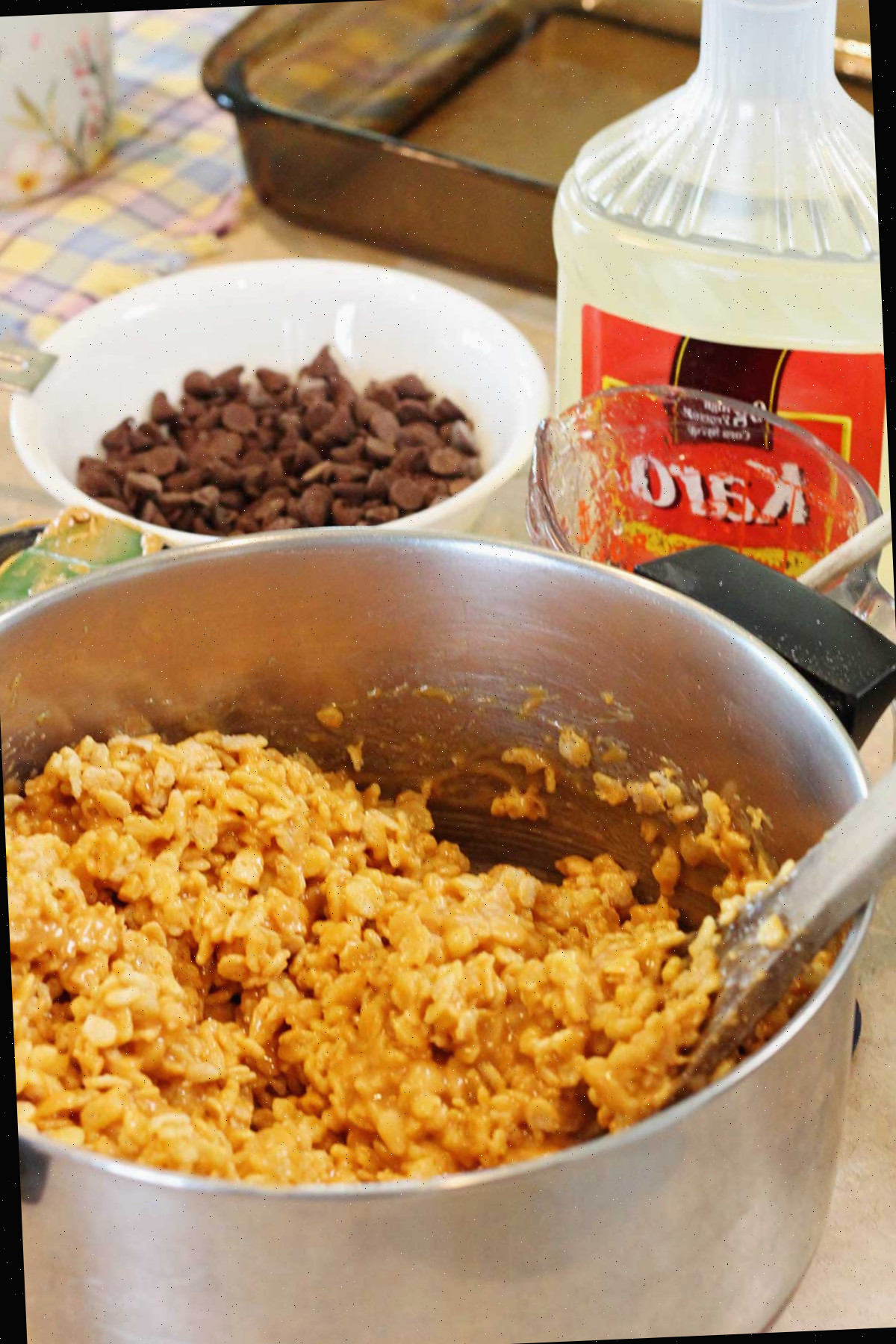 Mistura de arroz crocante em uma panela com gotas de chocolate e xarope Karo ao lado.