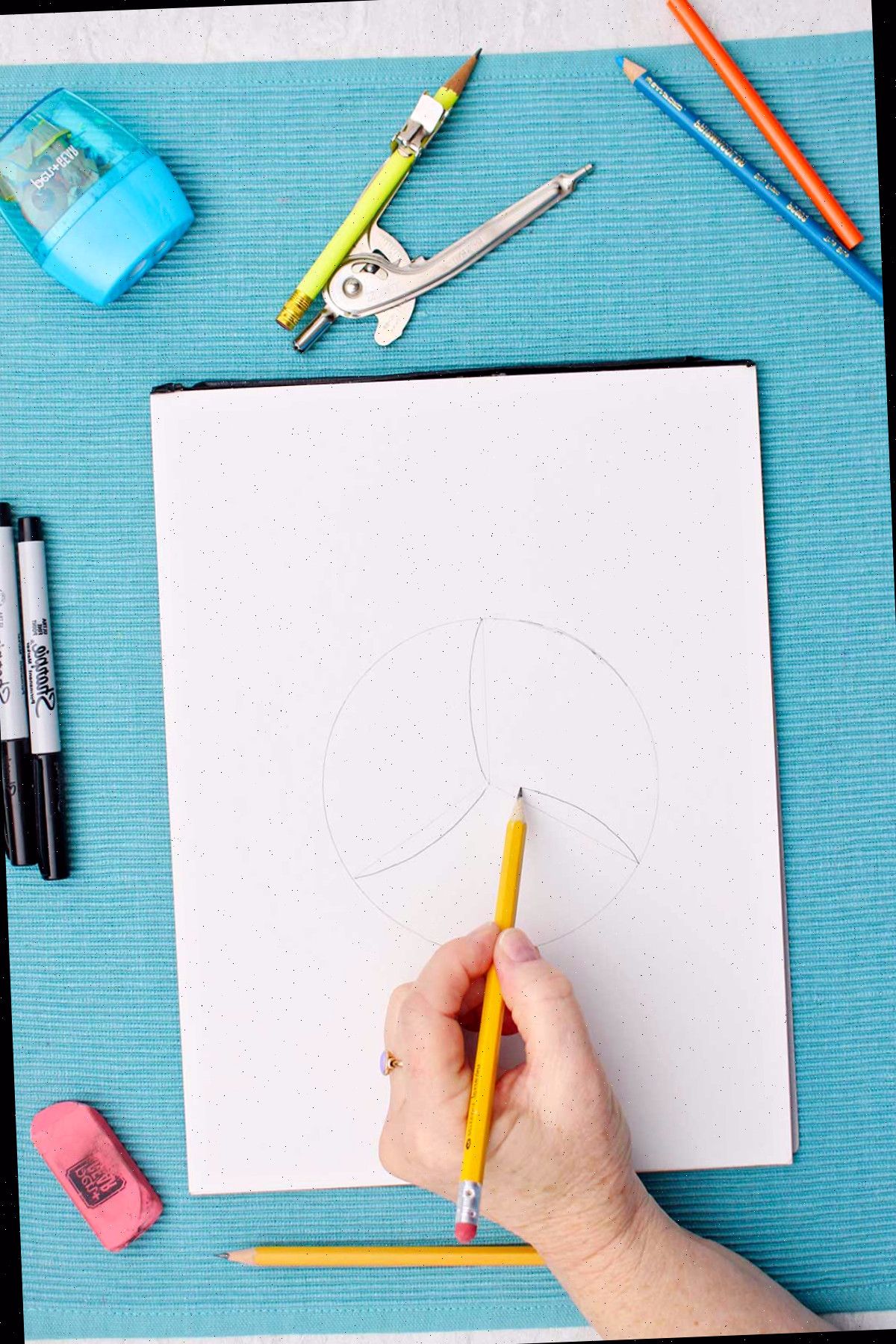 Pessoa esboçando detalhes do desenho do vôlei com um lápis.