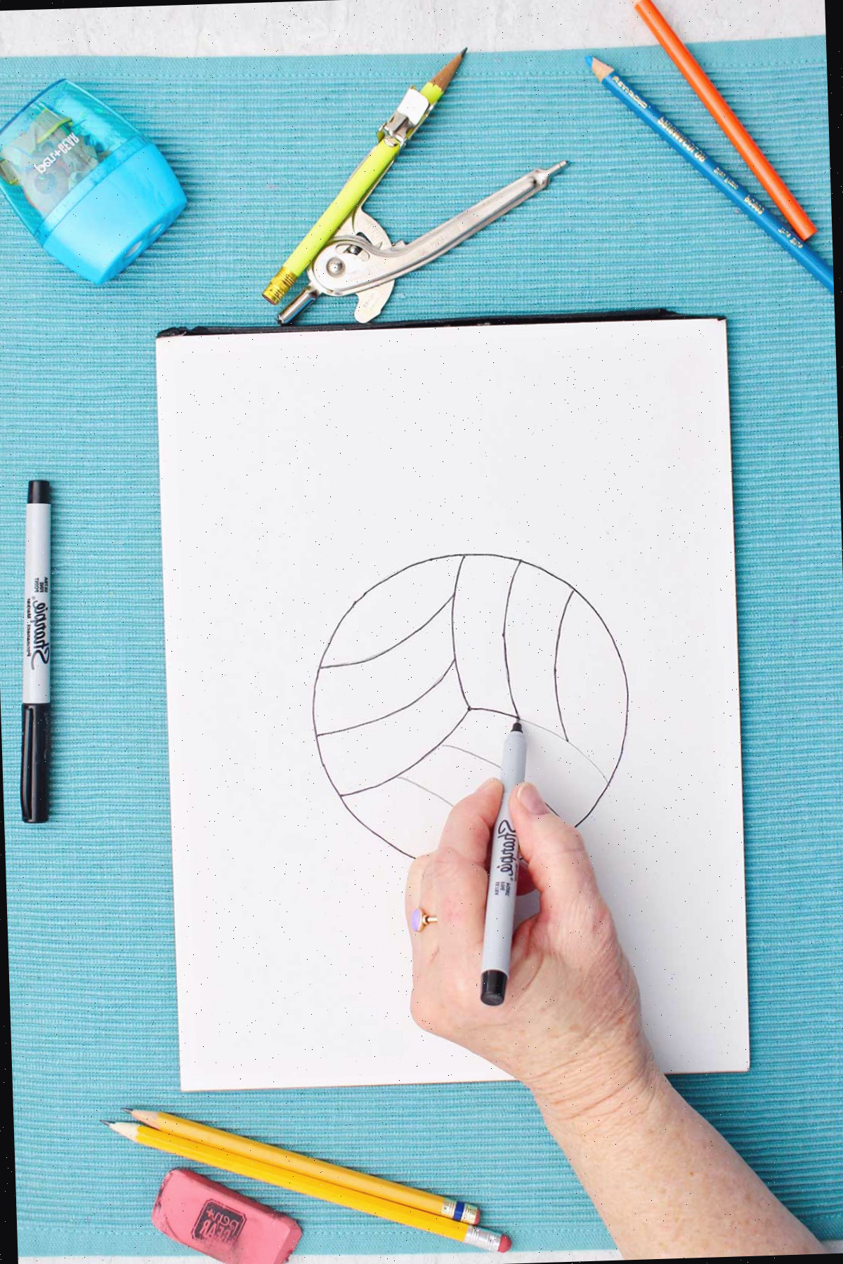 Uma pessoa contornando as linhas de lápis com um marcador no desenho de vôlei.