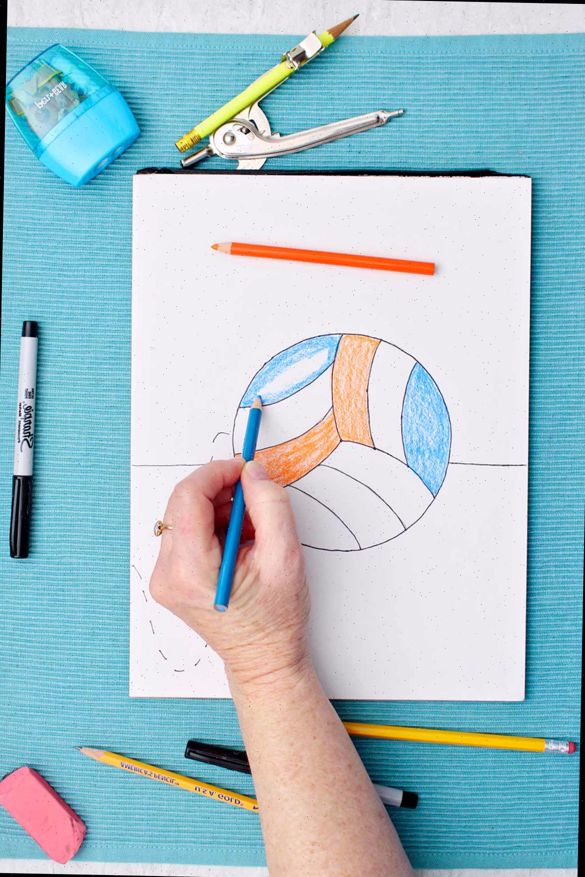 Pessoa colorindo um esboço de um vôlei com um lápis azul.