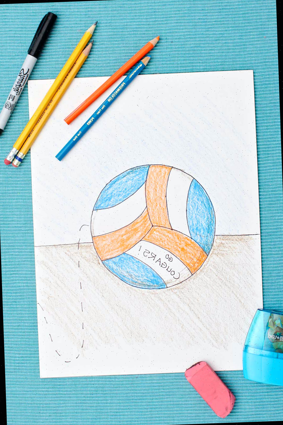 Desenho de vôlei multicolorido com lápis azuis e laranja com materiais próximos em um jogo americano azul.