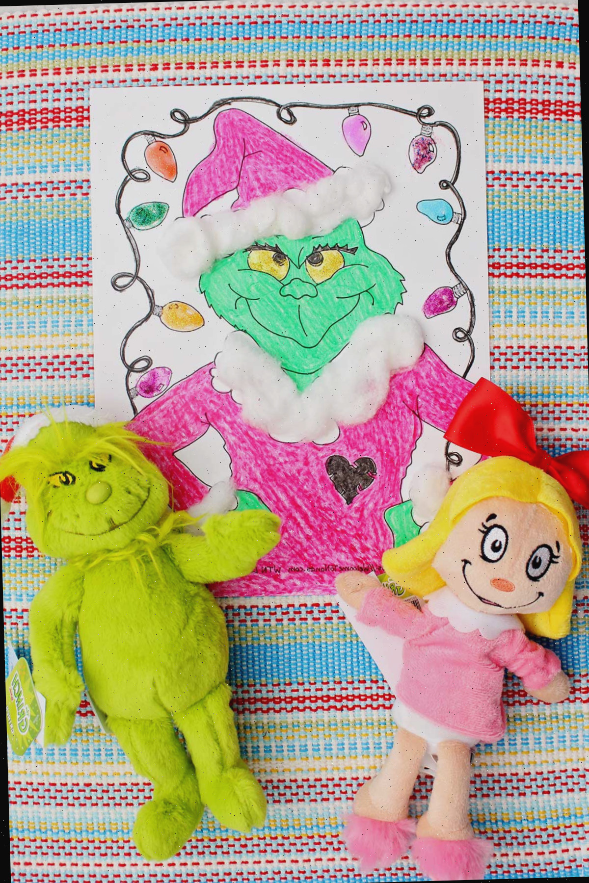 Página para colorir do Grinch finalizada com dois bichos de pelúcia do Grinch ao lado.
