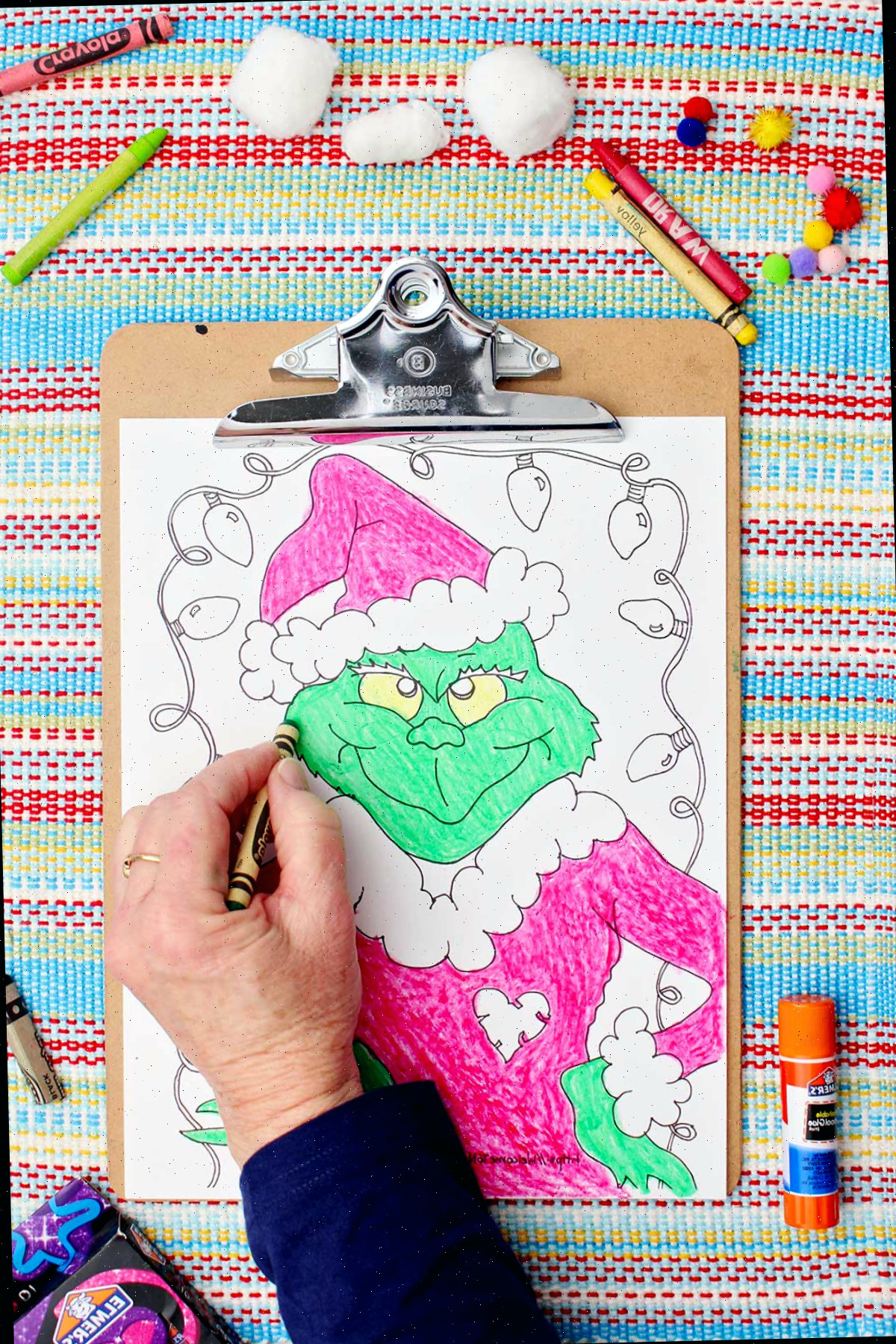Indivíduo colorindo o Grinch de verde na folha de colorir.