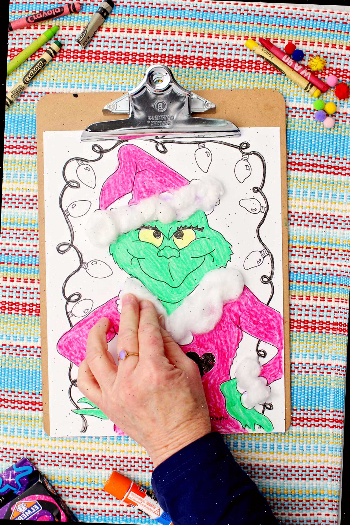 Indivíduo aplicando bolas de algodão nos detalhes do manto do Papai Noel na folha de colorir do Grinch.