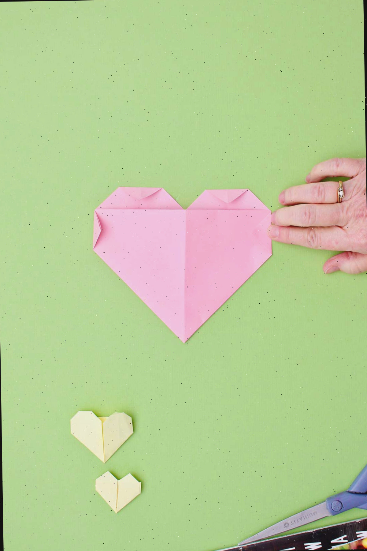 Uma pessoa dobrando os triângulos laterais para finalizar seu coração de origami.