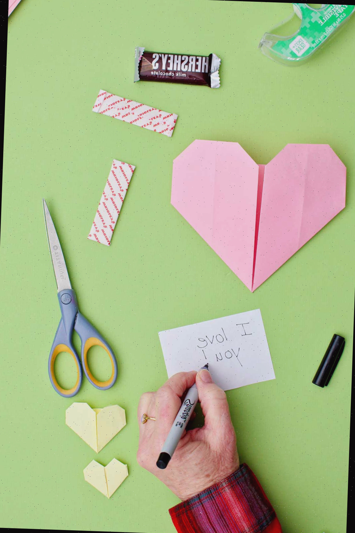 Uma pessoa escrevendo uma nota dizendo "Eu te amo!" para inserir em um coração de origami rosa.