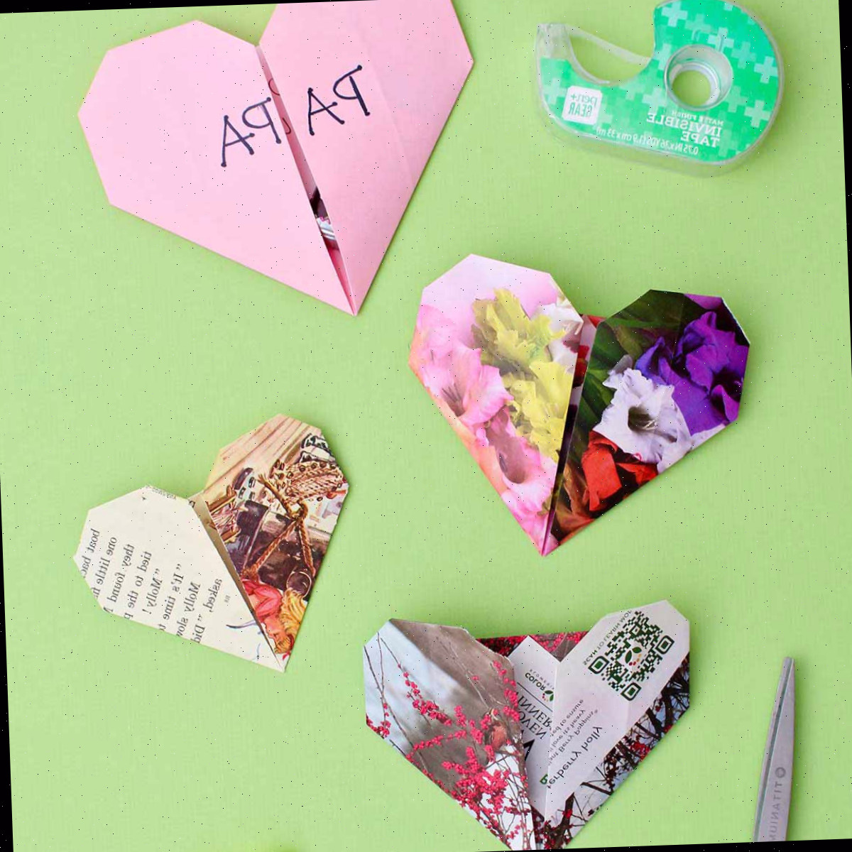 Quatro corações de origami em um fundo verde com tesoura e fita nas proximidades.
