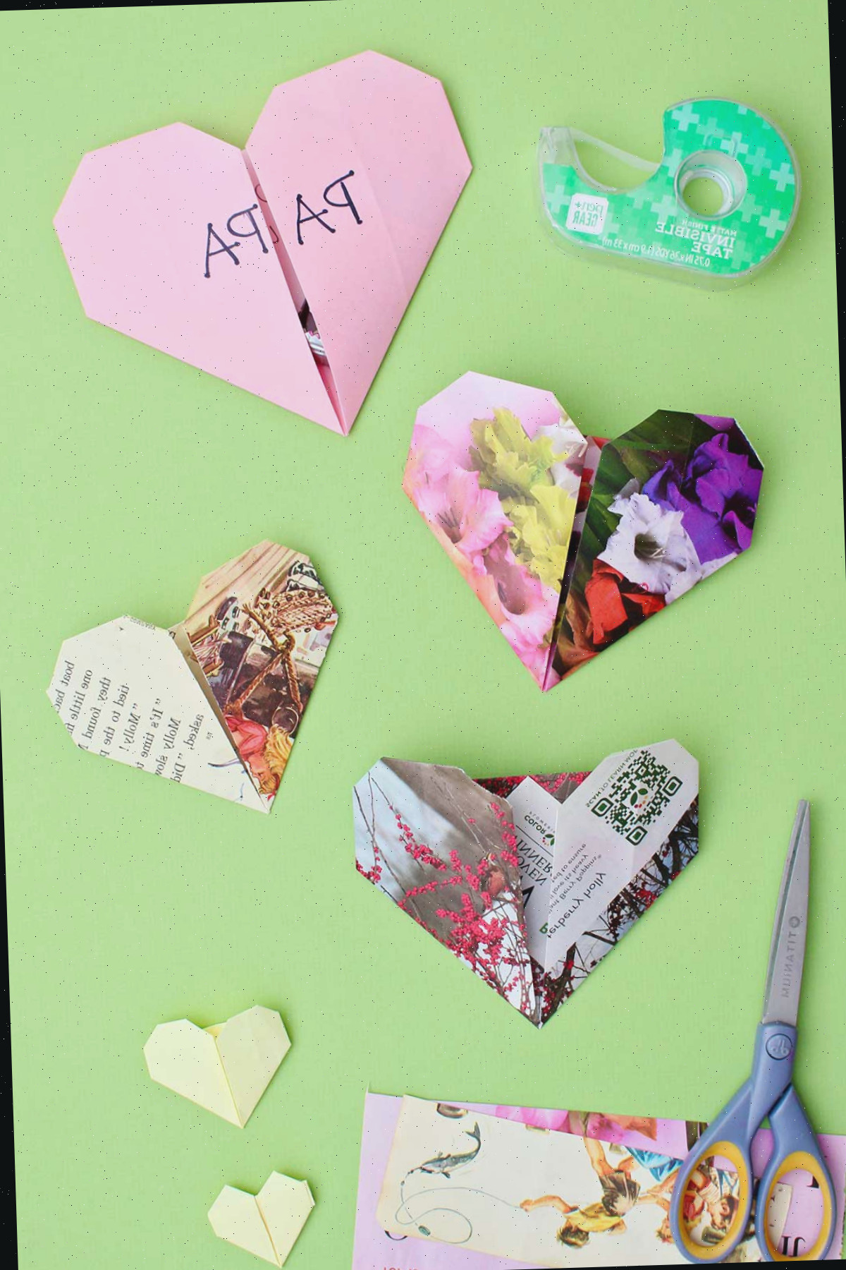 Quatro corações de origami em um fundo verde com tesouras e fita por perto.