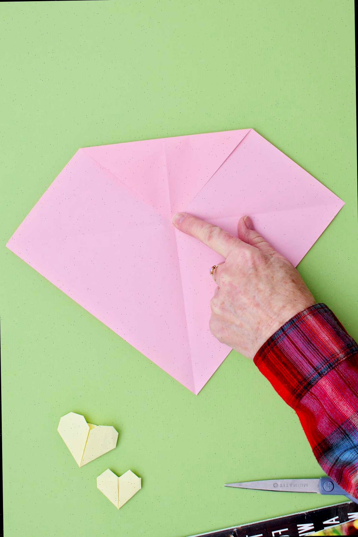 Dobrando o canto superior de um pedaço de papel rosa para baixo em direção ao centro para criar a parte superior de um coração.