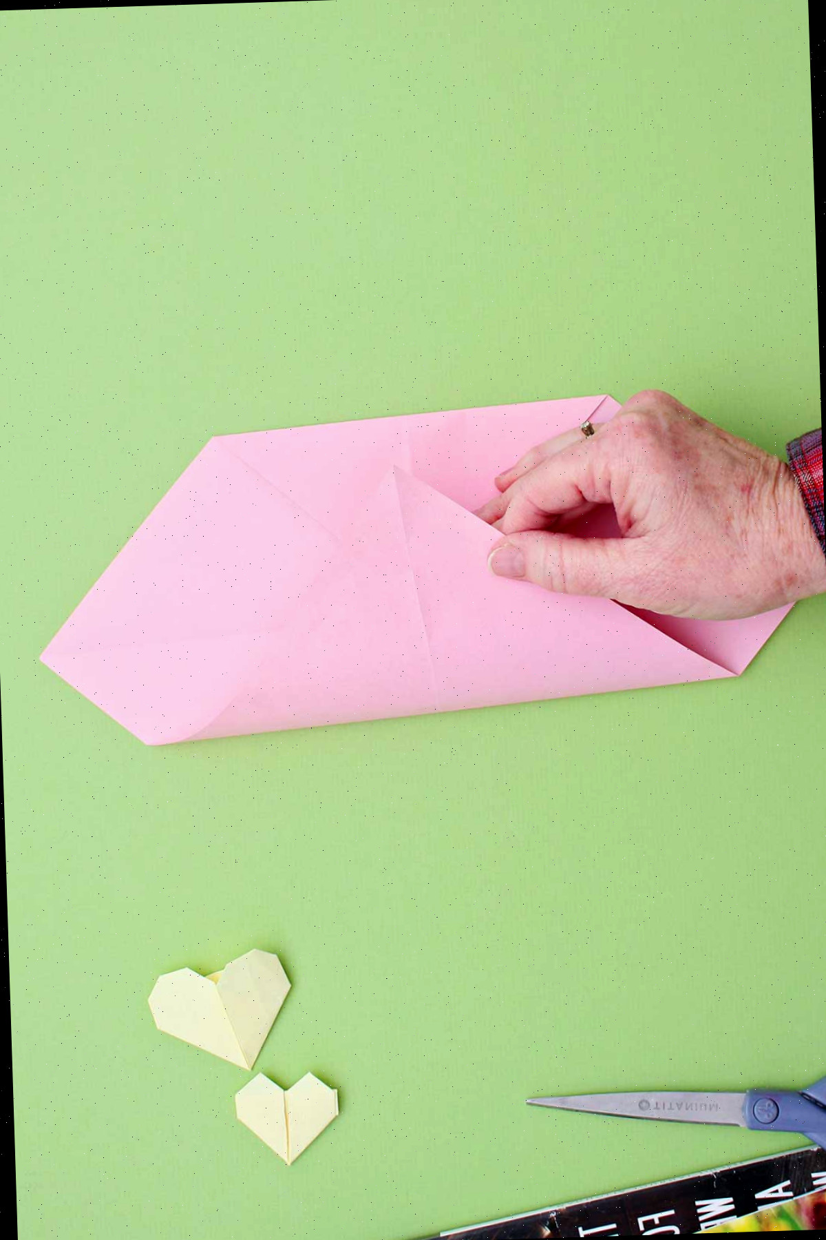 Indivíduo dobrando o canto de uma folha de papel rosa para encontrar a parte superior dobrada.