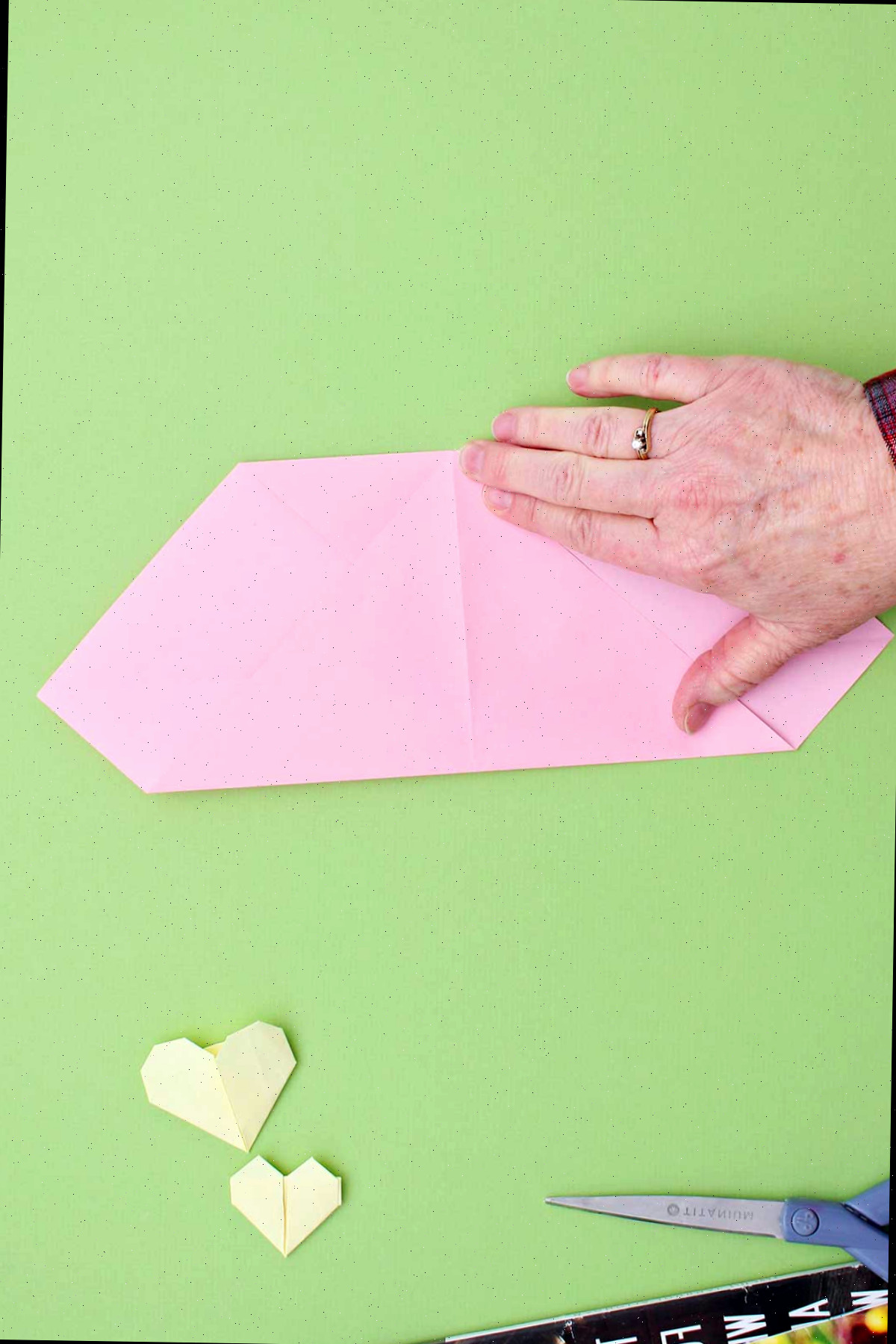 Indivíduo dobrando o canto de uma folha de papel rosa para cima para encontrar a parte superior dobrada.