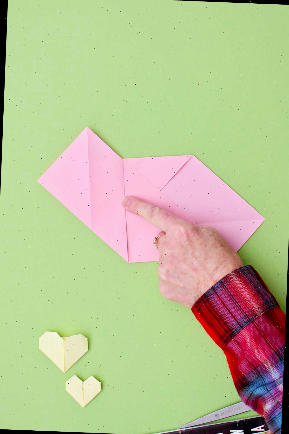 Indivíduo exibindo um coração de origami rosa com um vinco central.