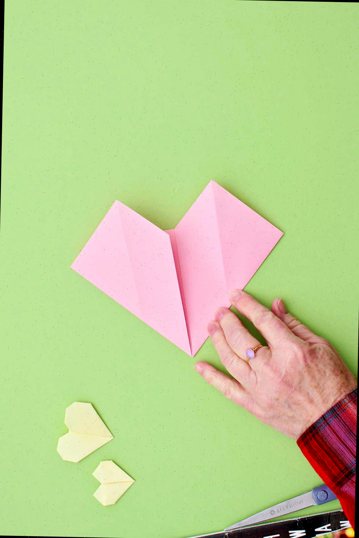Uma pessoa dobrando as laterais para criar a forma do coração de origami.