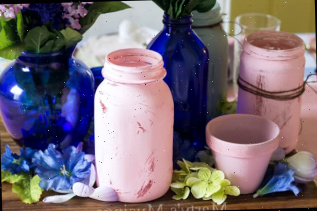 Uma xícara de café e um vaso de flores sobre uma mesa, com um pote mason jar