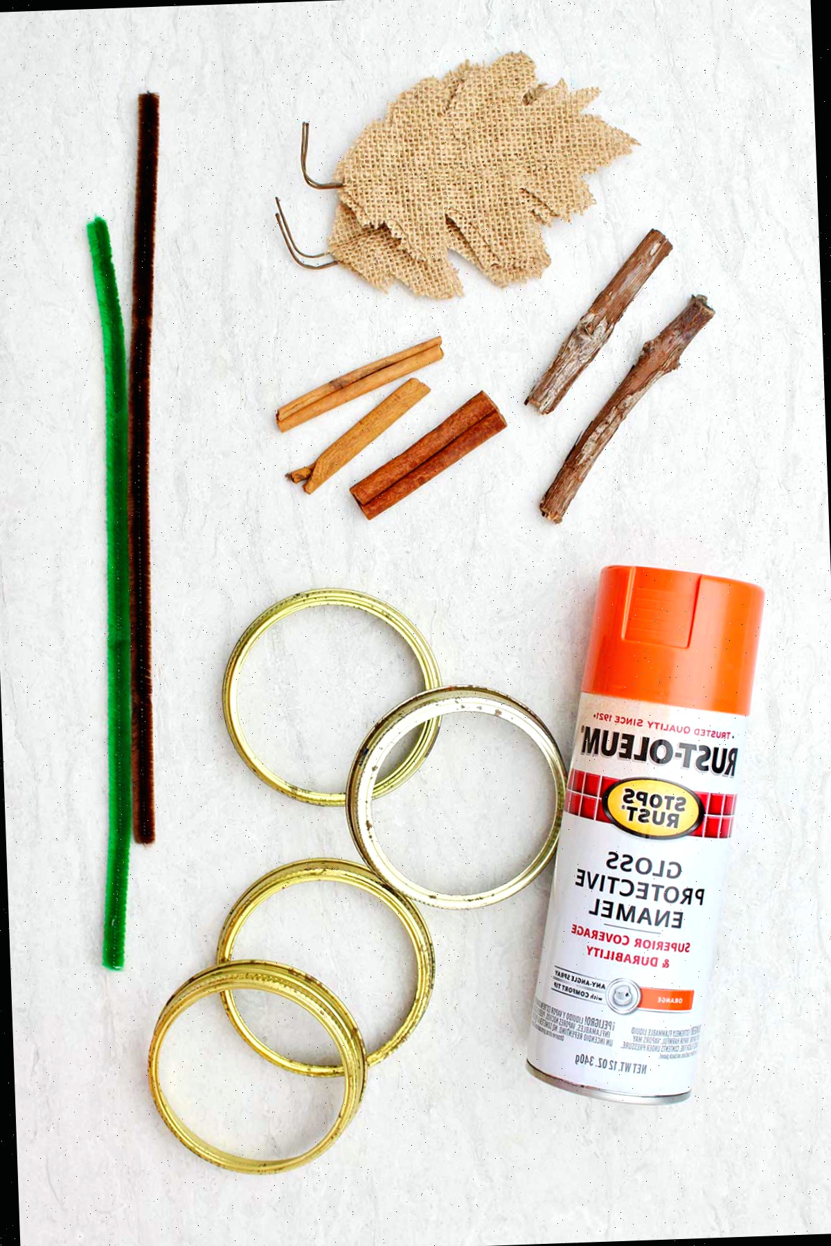 Materiais necessários para confeccionar abóboras de tampas de pote de conserva: folhas de juta, gravetos, paus de canela, tinta spray, tampas de pote de conserva e limpadores de pipe.