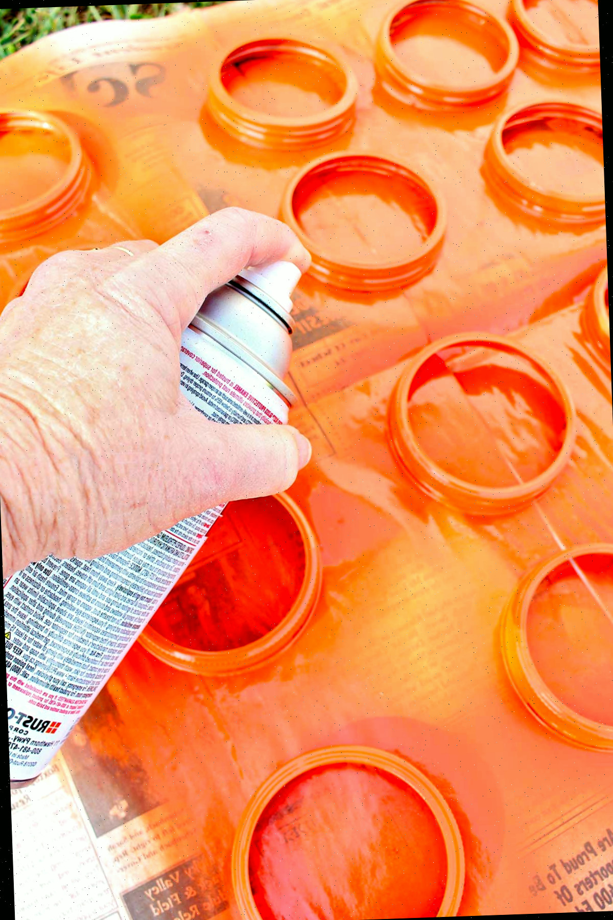 Indivíduo pintando tampa de pote de conserva laranja do lado externo em um pedaço de papel jornal.